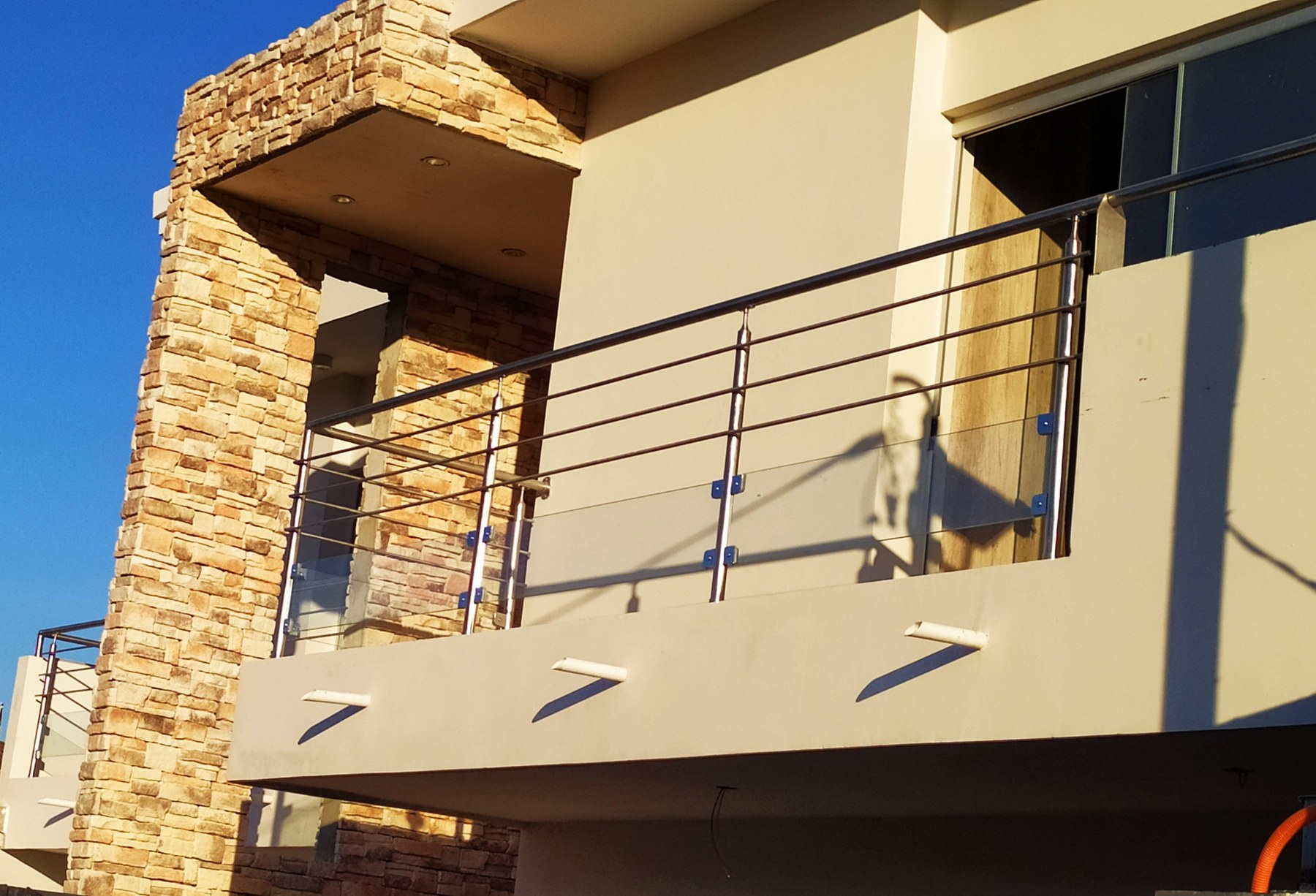 Baranda de acero inoxidable en el balcón de una casa con revestimiento de piedra · MÁS VIDRIOS