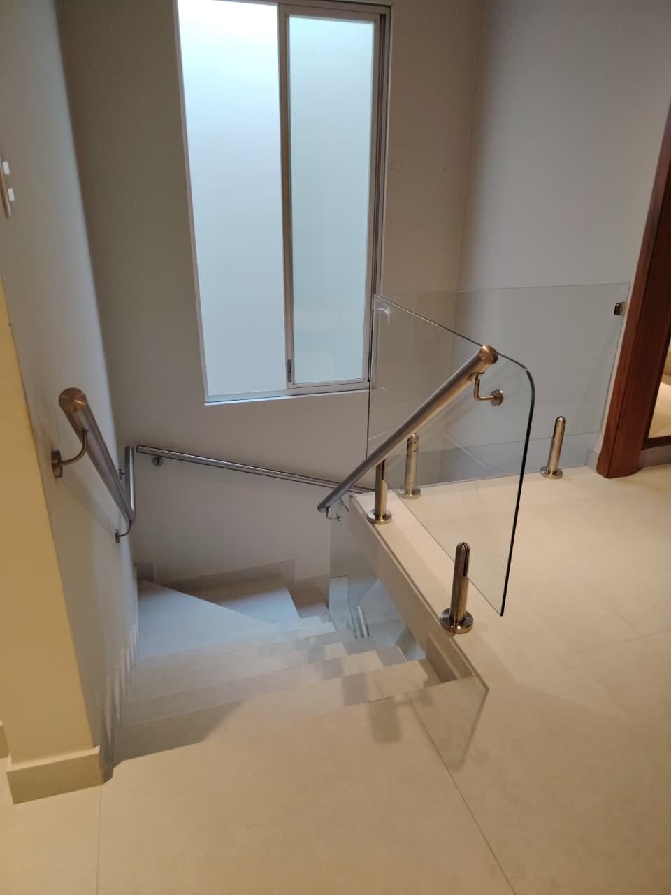 Baranda de vidrio curvo con parantes y pasamanos de acero inoxidable en escalera interior · MÁS VIDRIOS