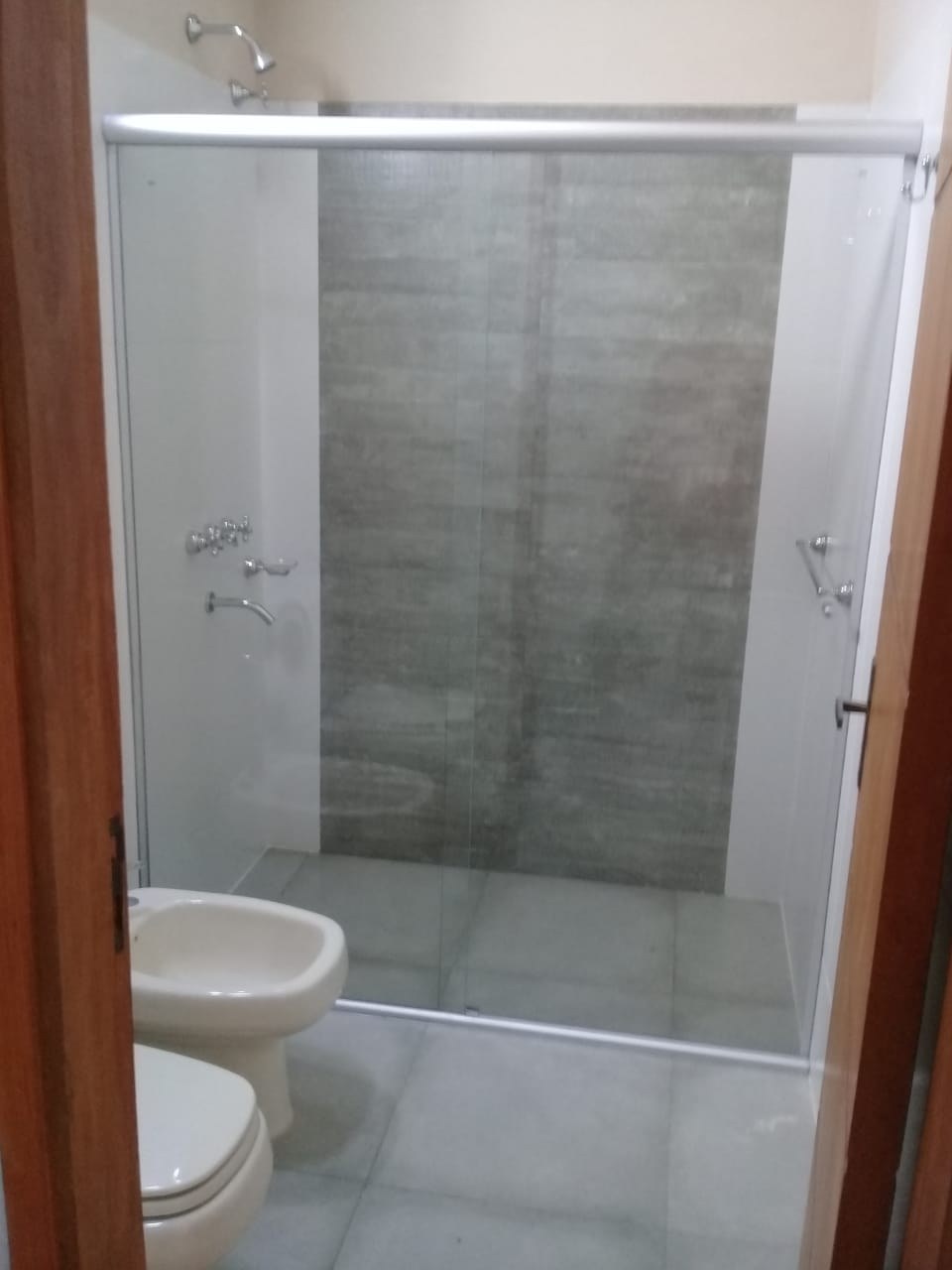 Box de ducha corredizo de vidrio transparente en baño con revestimiento gris · MÁS VIDRIOS
