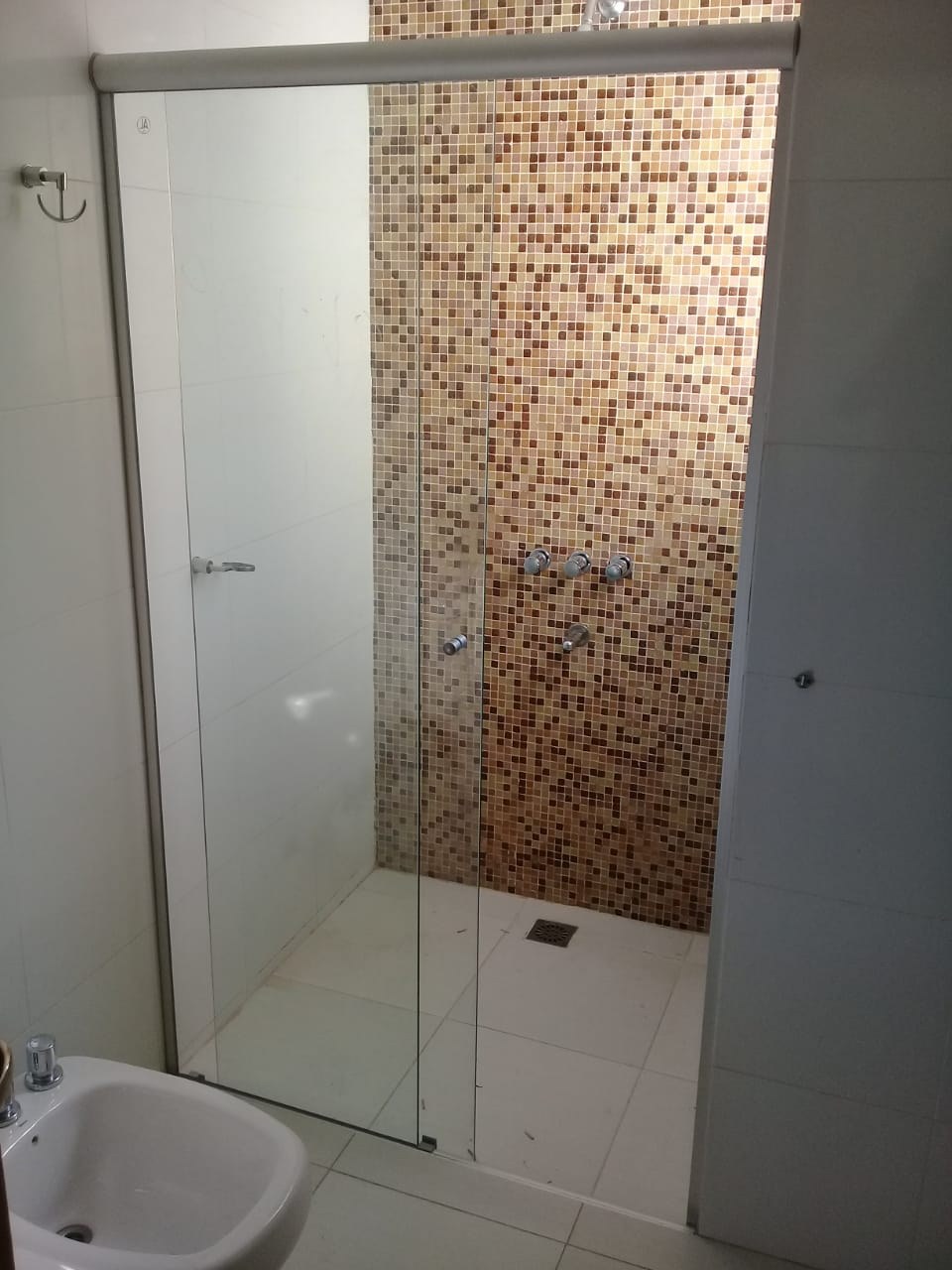Box de ducha corredizo en vidrio transparente sobre pared de mosaicos cobre · MÁS VIDRIOS