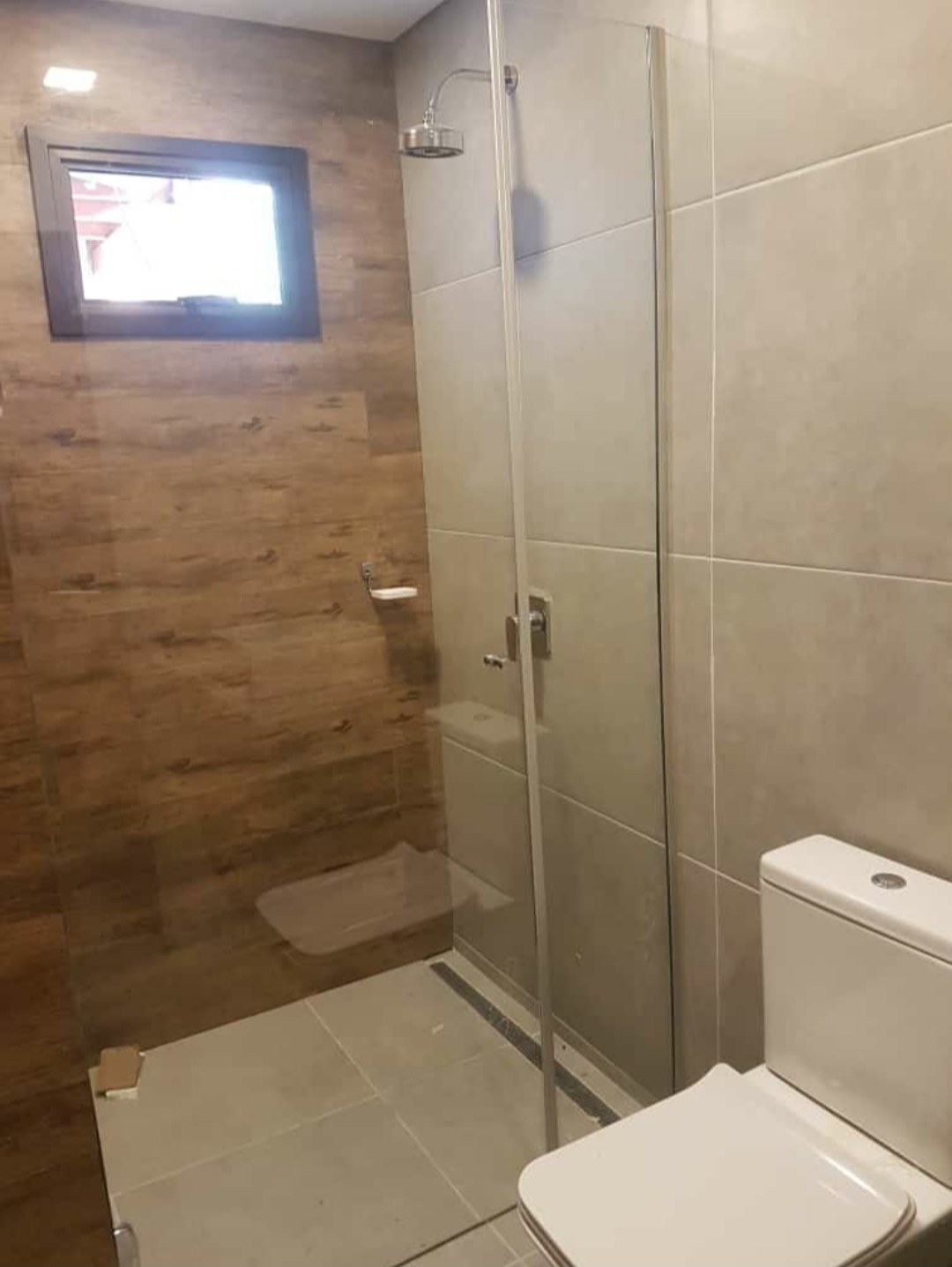 Box de ducha recto en vidrio transparente en baño con pared símil madera · MÁS VIDRIOS