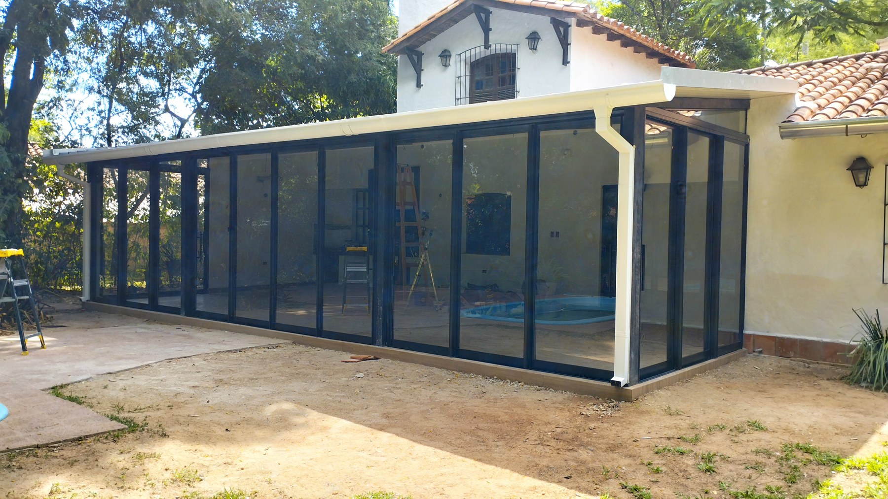 Cerramiento de patio con pileta en vidrio y perfilería de aluminio negra con techo inclinado · MÁS VIDRIOS