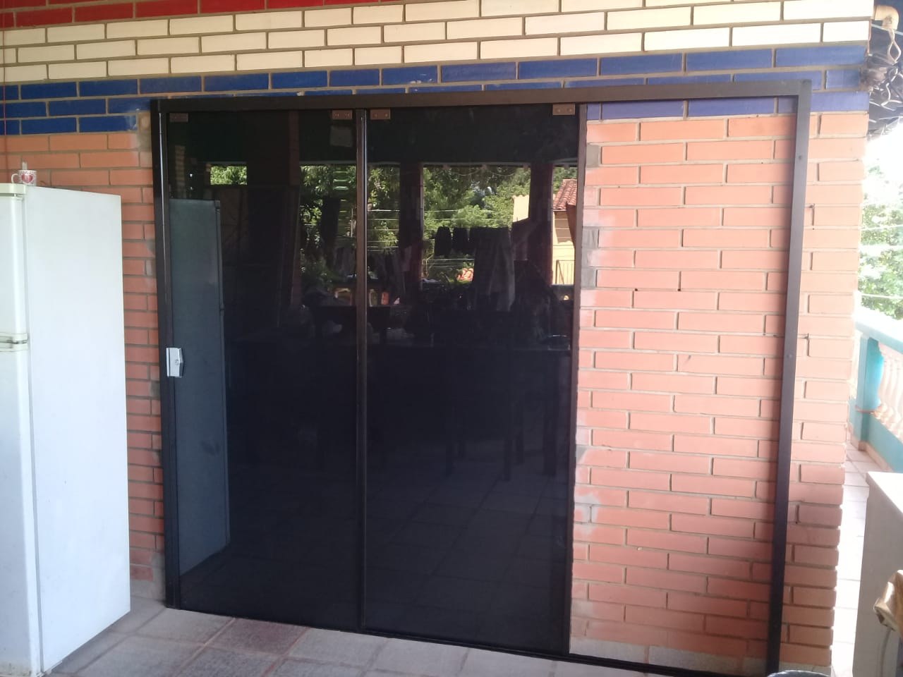 Puerta corrediza de cuatro hojas con vidrio oscuro en galería de ladrillo · MÁS VIDRIOS