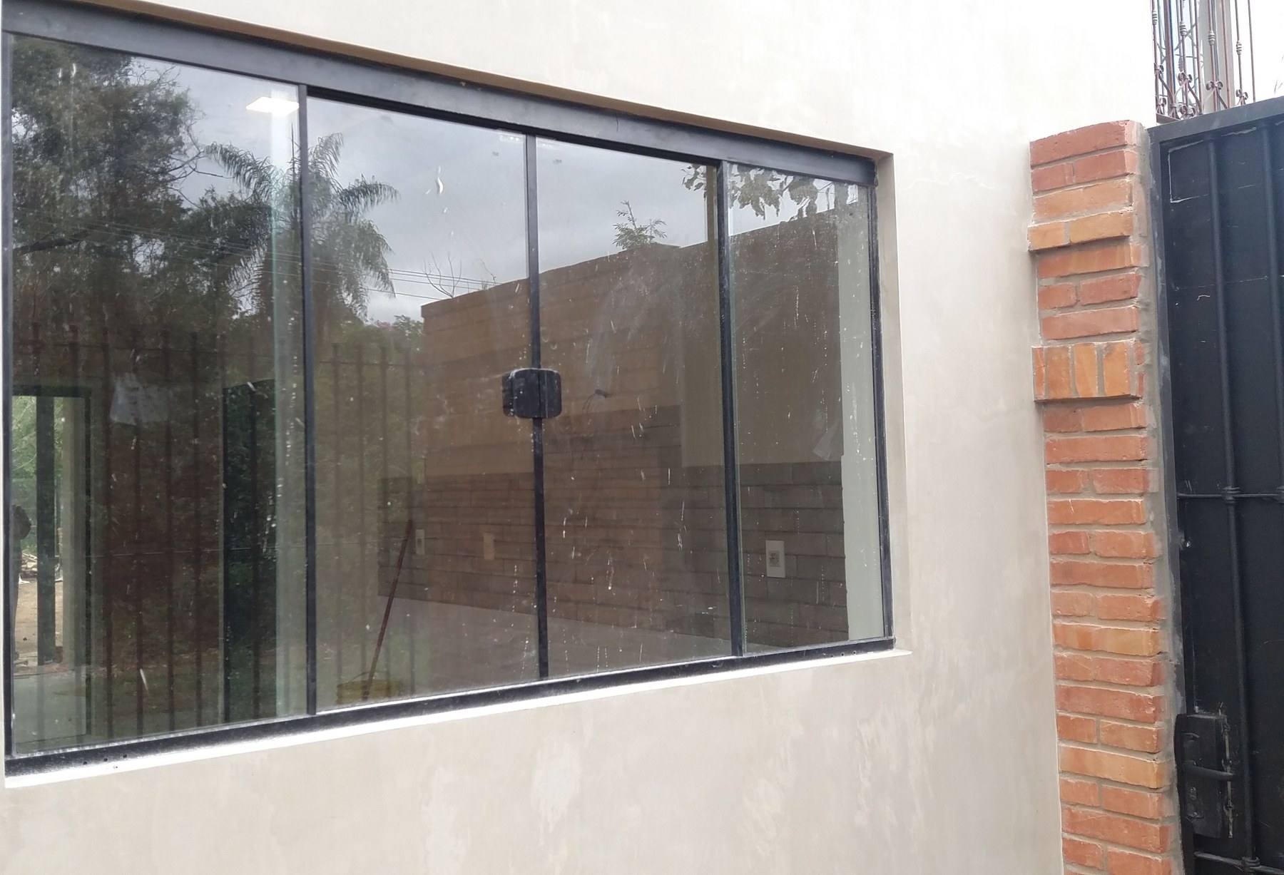 Ventana corrediza de aluminio oscuro en la pared blanca de una vivienda · MÁS VIDRIOS