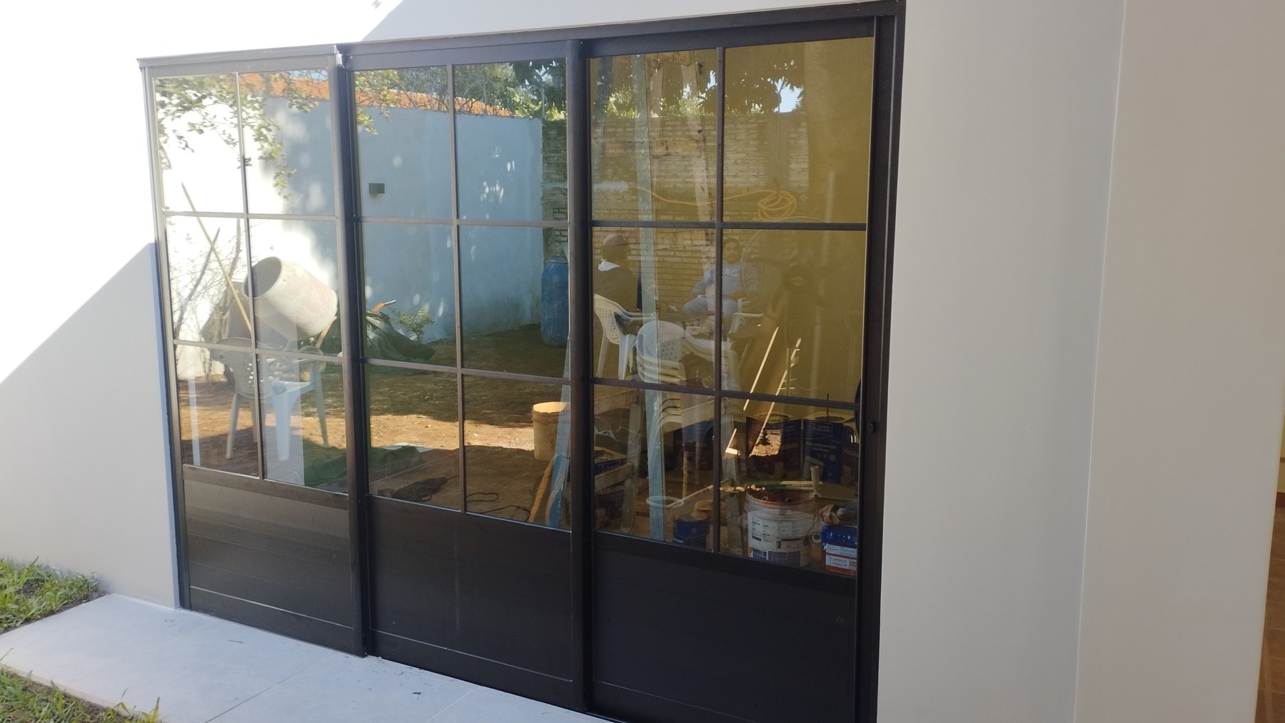 Cerramiento de galería con paños corredizos cuadrillé de aluminio negro visto desde el jardín · MÁS VIDRIOS