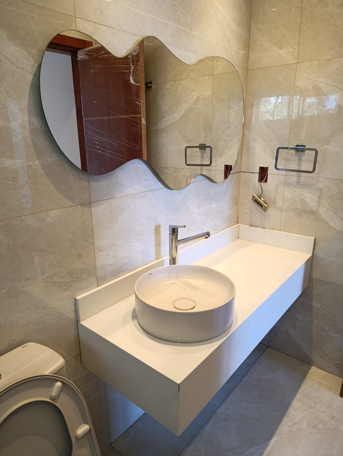 Espejo de diseño orgánico sobre bacha flotante en baño con revestimiento símil mármol · MÁS VIDRIOS