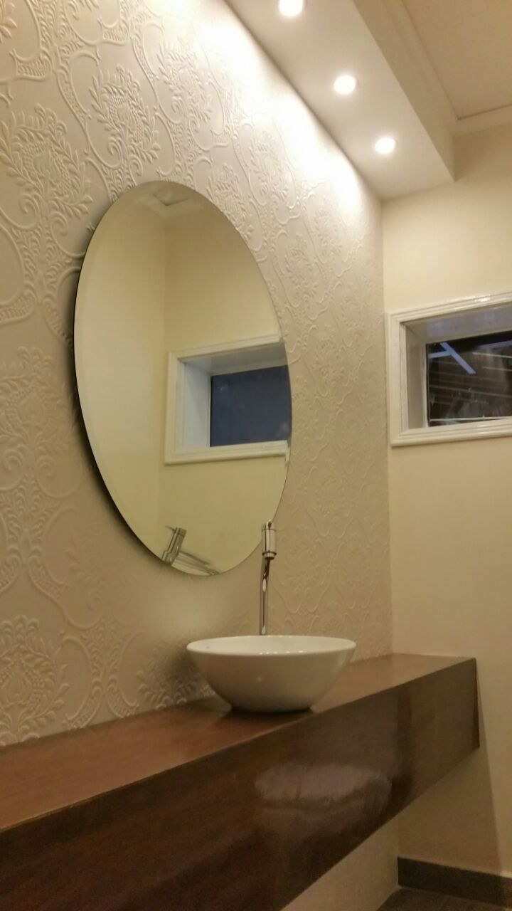 Espejo oval sobre mesada de madera en toilette con pared texturada · MÁS VIDRIOS