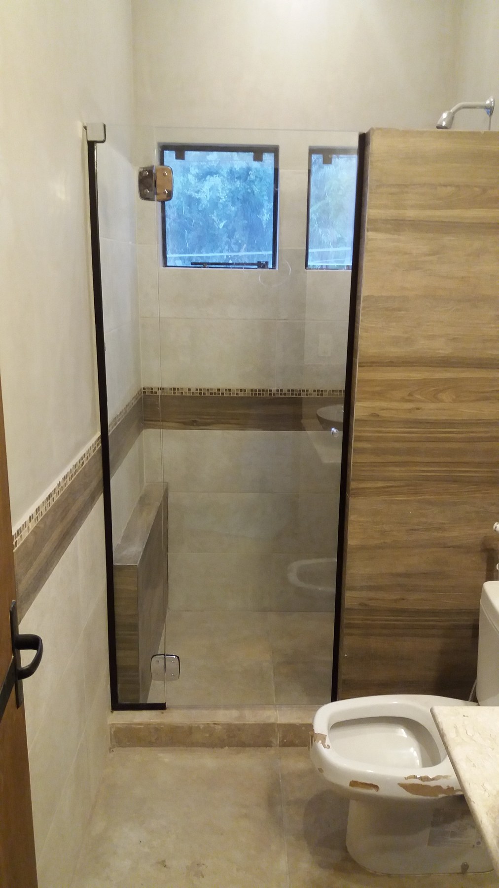 Mampara de ducha de vidrio con perfilería negra en baño con revestimiento símil madera · MÁS VIDRIOS