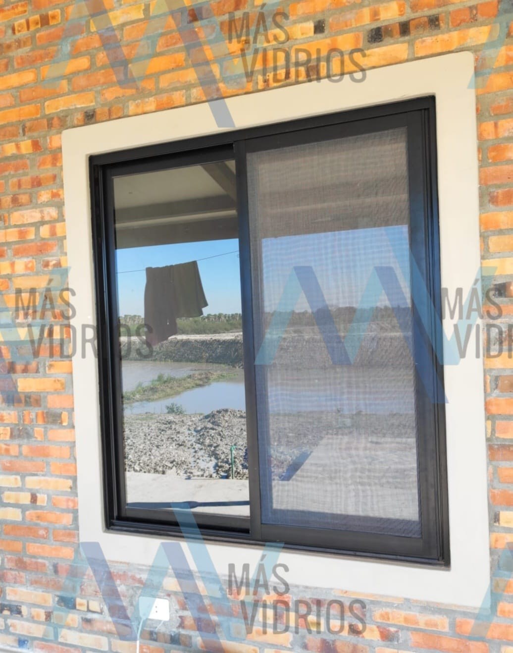 Ventana corrediza de aluminio negro con mosquitero corredizo en pared de ladrillo visto · MÁS VIDRIOS