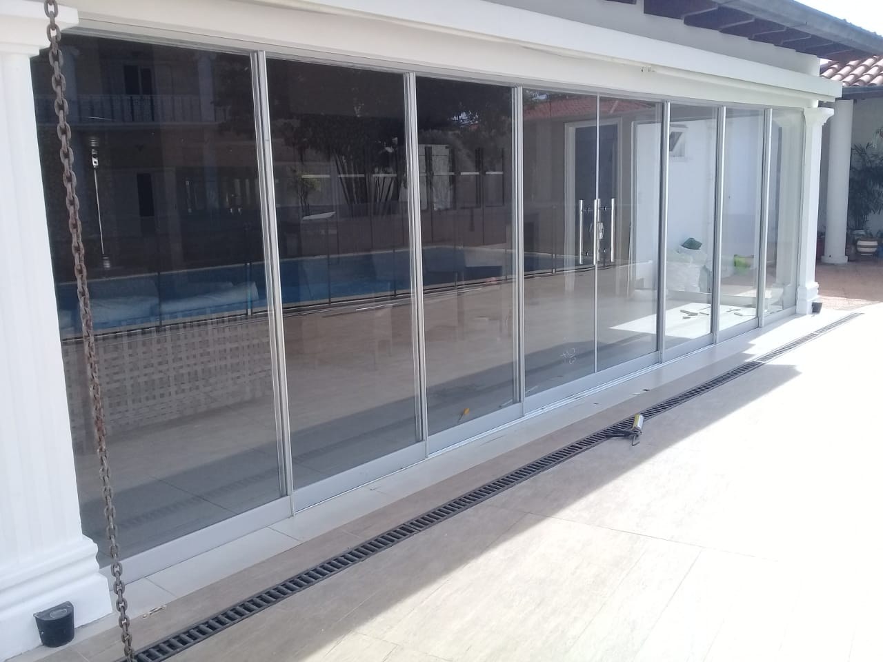 Cerramiento de paneles corredizos Novaslider cerrado en galería frente a la piscina · MÁS VIDRIOS