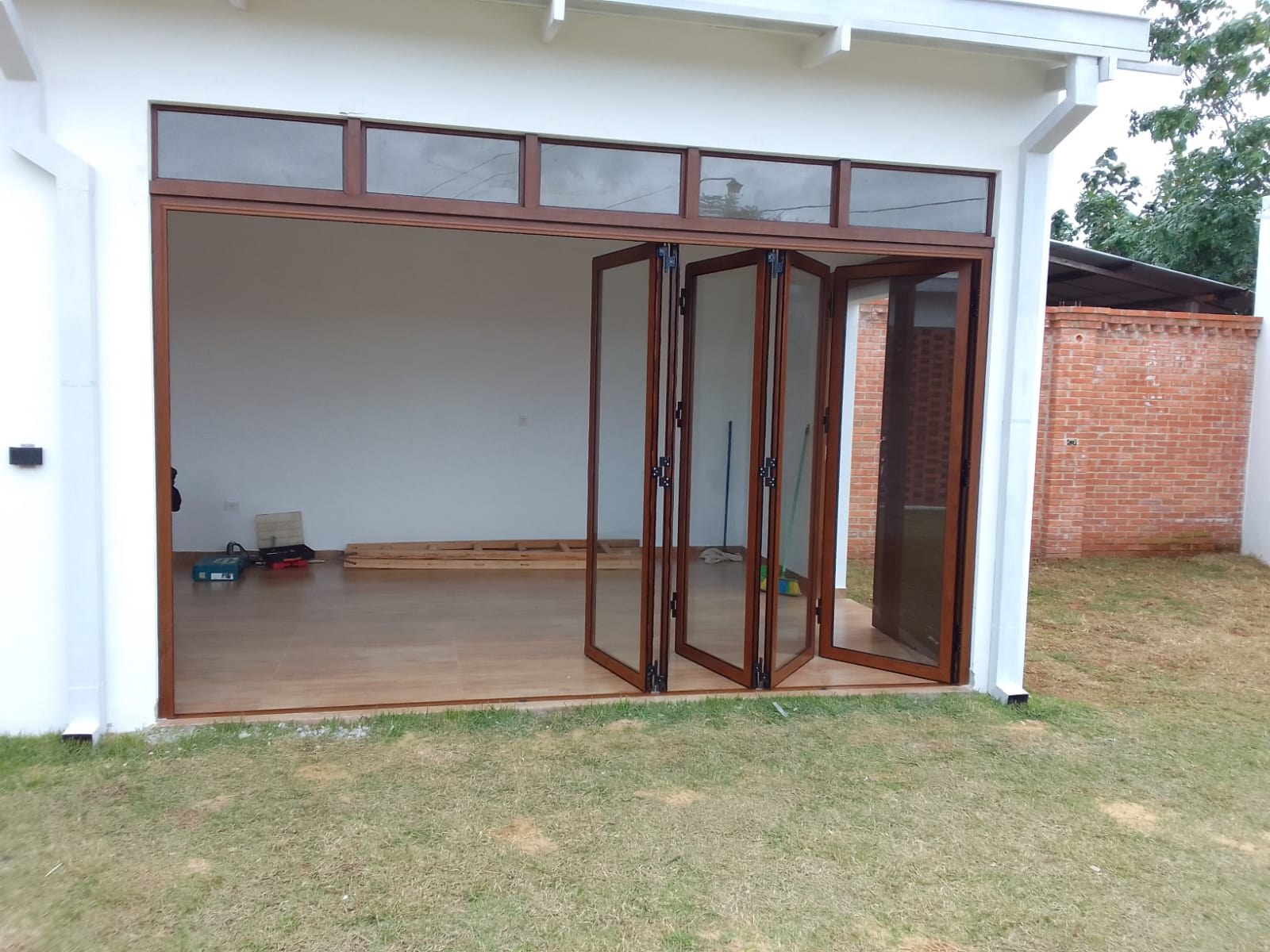 Puerta plegadiza de aluminio símil madera a medio plegar en cerramiento de quincho · MÁS VIDRIOS