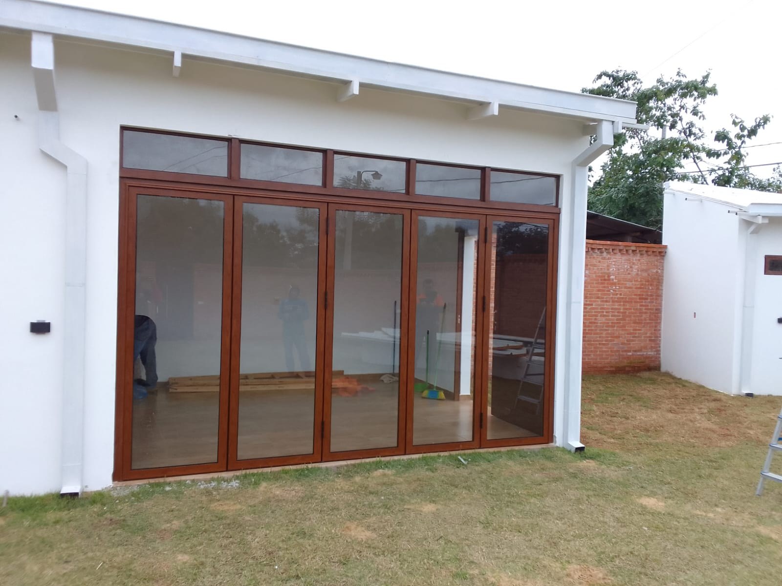 Puerta plegadiza de aluminio símil madera cerrada con paños fijos superiores en quincho · MÁS VIDRIOS