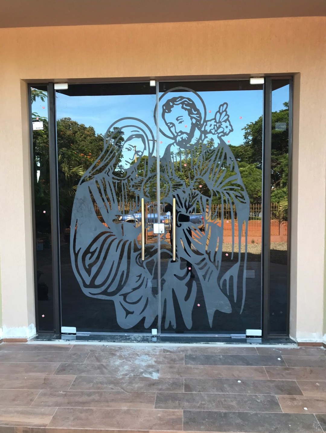 Puerta doble de vidrio con ploteado de figura religiosa en el acceso · MÁS VIDRIOS