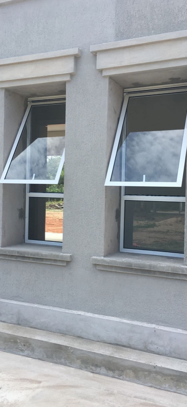 Ventanas proyectantes de aluminio abiertas en fachada gris · MÁS VIDRIOS