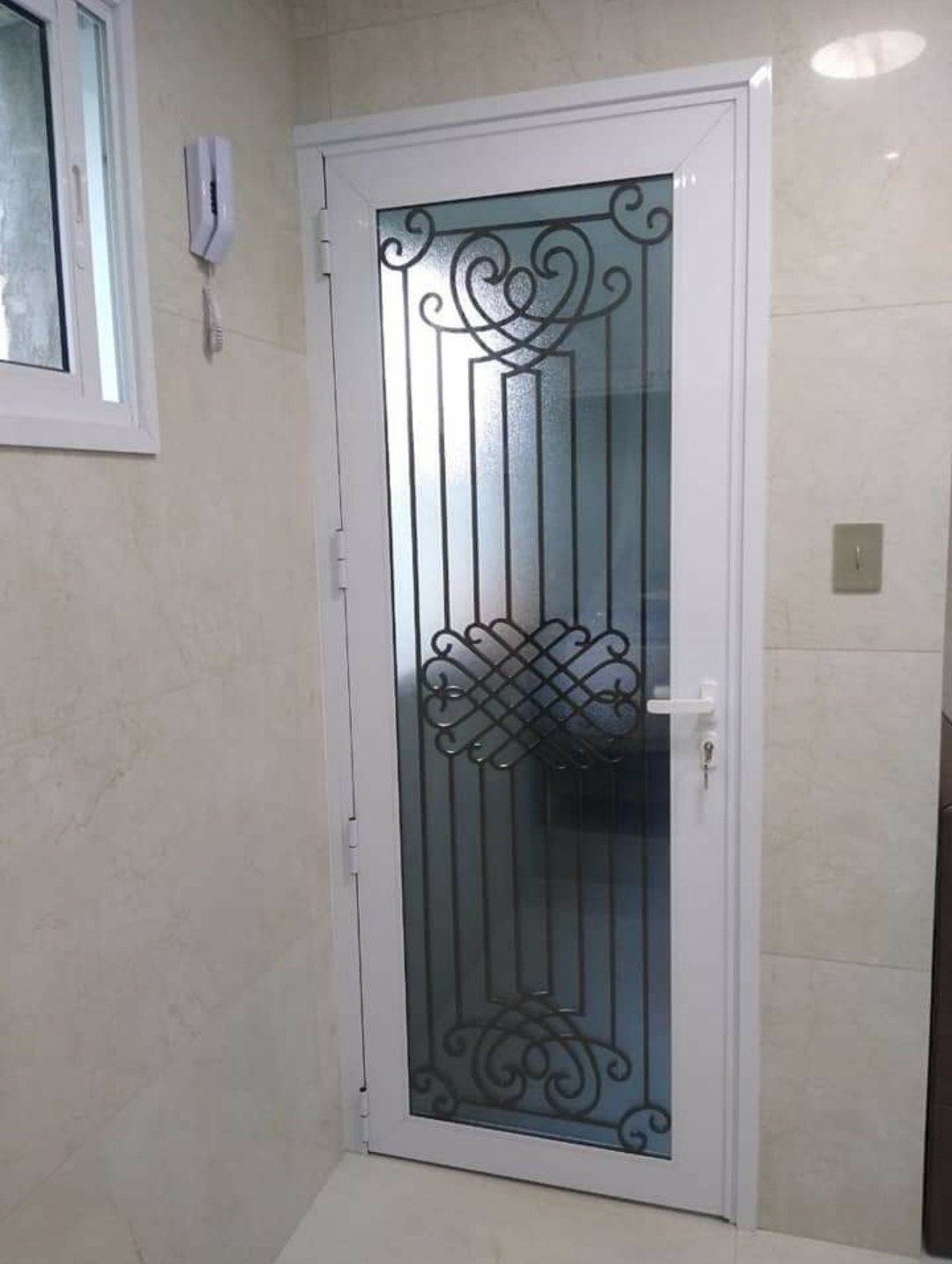 Puerta batiente de aluminio blanco con vidrio y reja artística en el ingreso de una casa · MÁS VIDRIOS