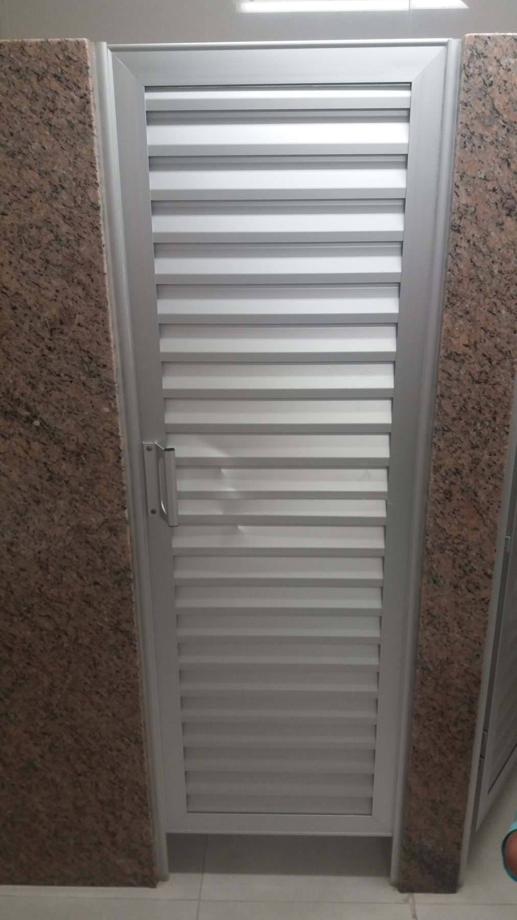 Puerta celosía de aluminio blanco en acceso a baño, entre paredes revestidas en granito · MÁS VIDRIOS