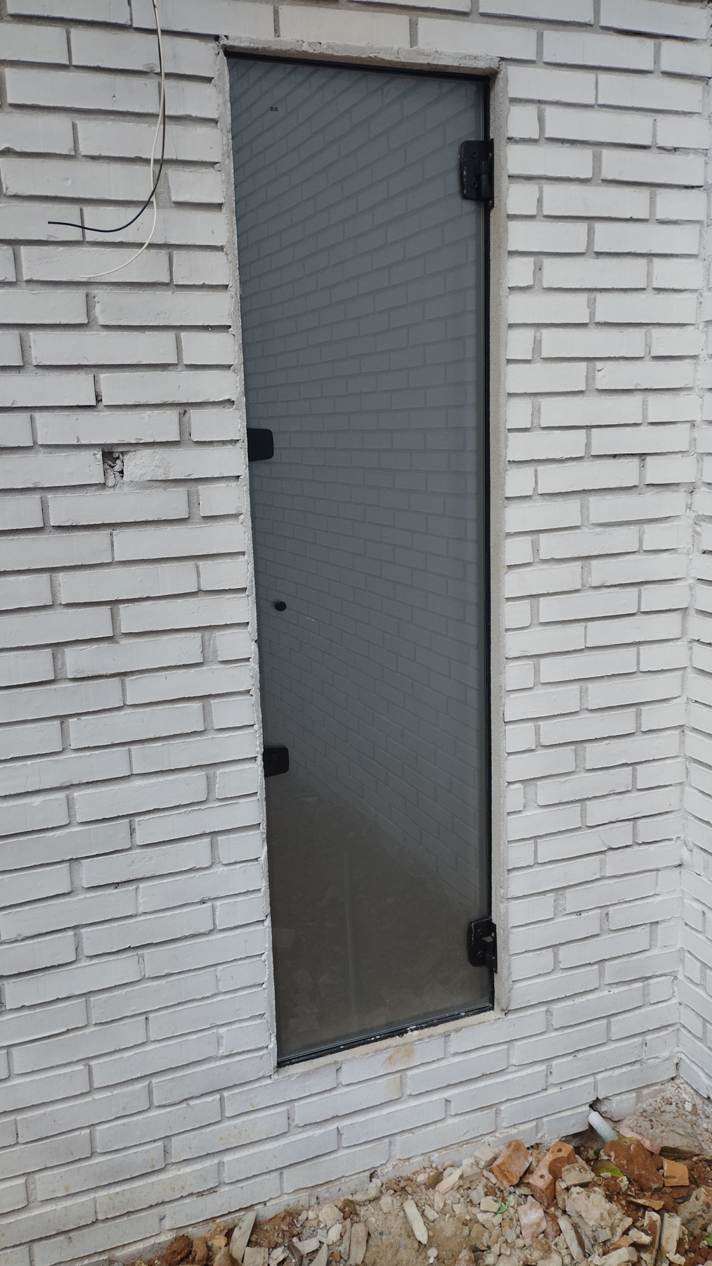 Puerta batiente de aluminio con paño de tejido en pared de ladrillo visto blanco · MÁS VIDRIOS