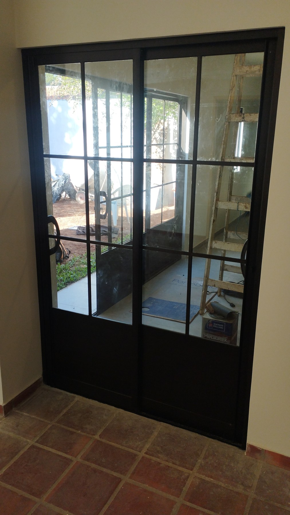 Puerta corrediza cuadrillé de aluminio negro de dos hojas sobre piso de baldosas cerámicas · MÁS VIDRIOS