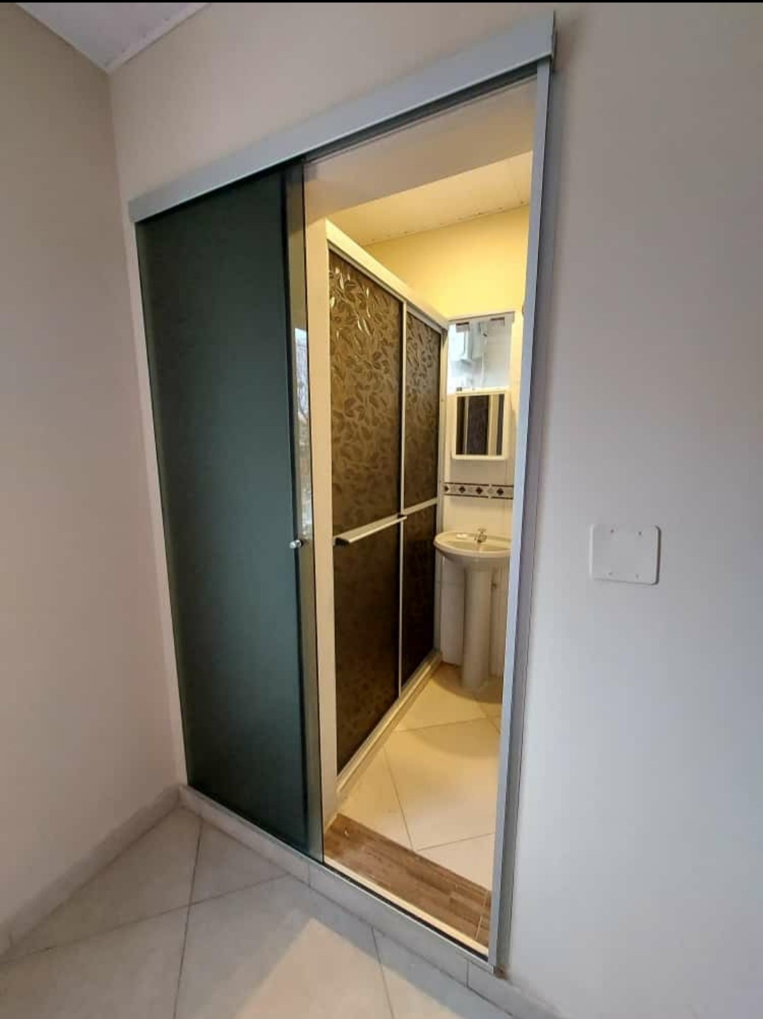 Puerta corrediza de aluminio con paño de vidrio oscuro en el acceso al baño · MÁS VIDRIOS