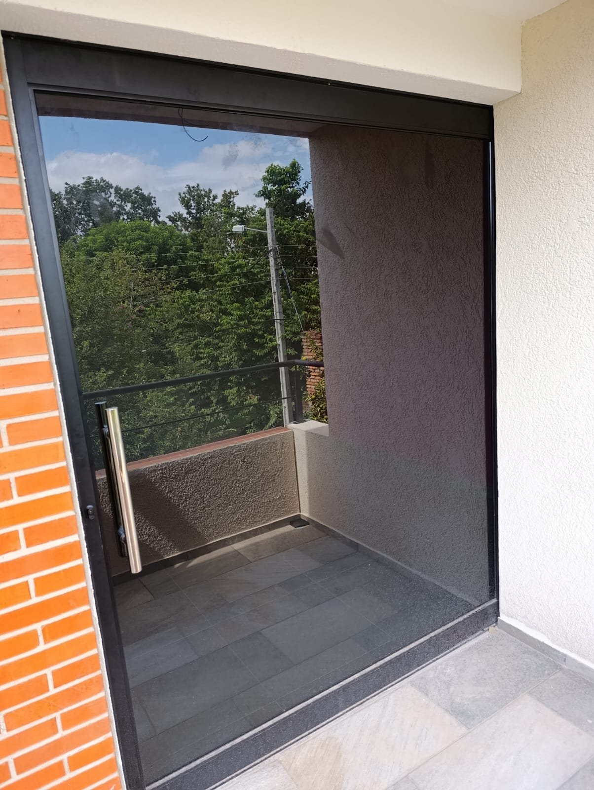 Puerta corrediza de vidrio fumé con barral de acero inoxidable en balcón · MÁS VIDRIOS