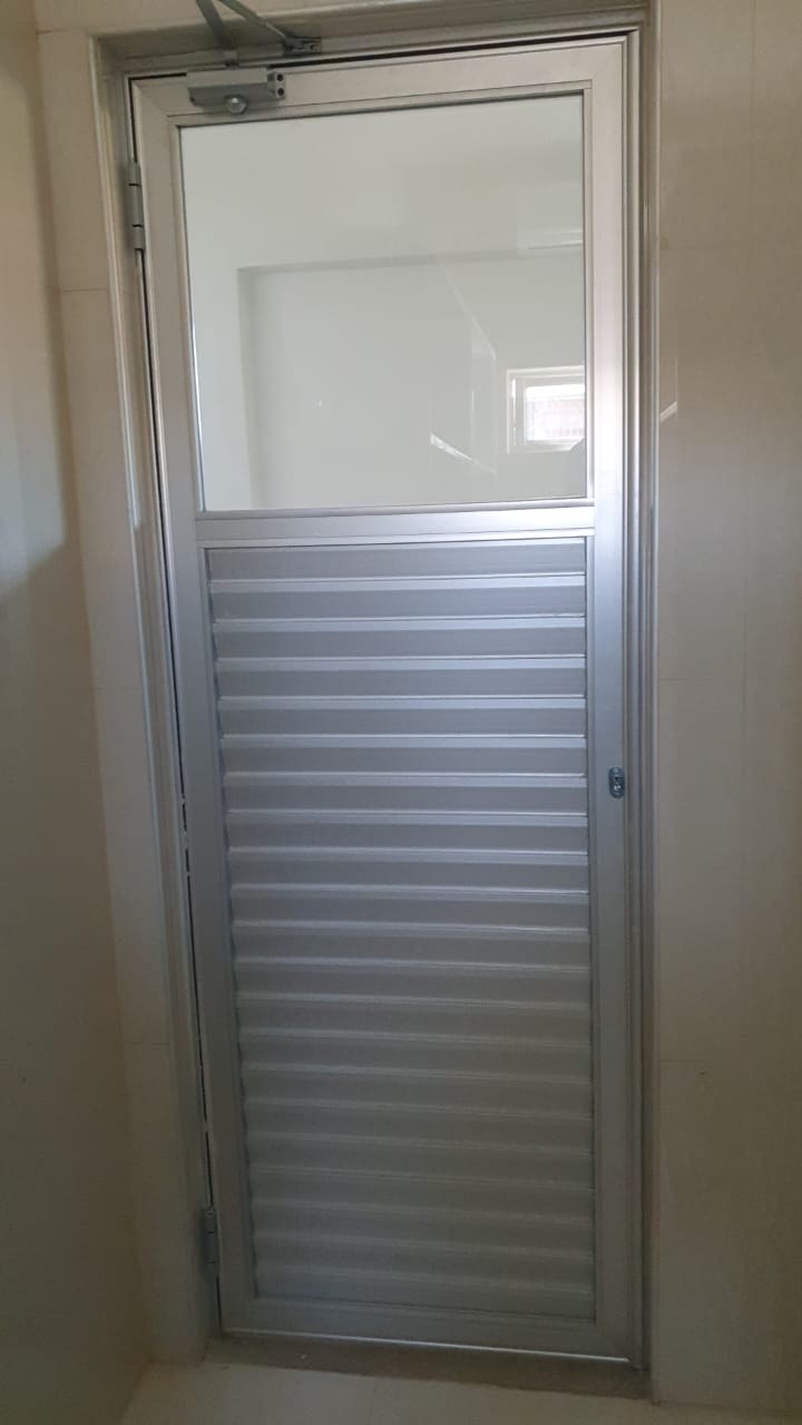 Puerta batiente de aluminio natural con paño de vidrio y celosía en la mitad inferior · MÁS VIDRIOS