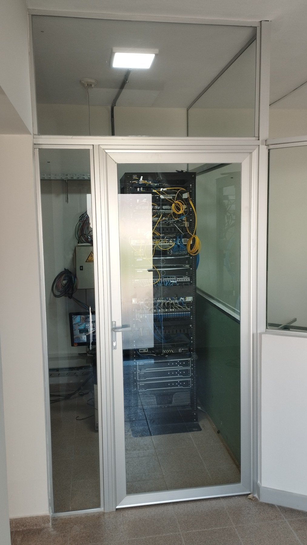Puerta batiente de aluminio blanco con vidrio integrada a tabiques vidriados de sala técnica · MÁS VIDRIOS