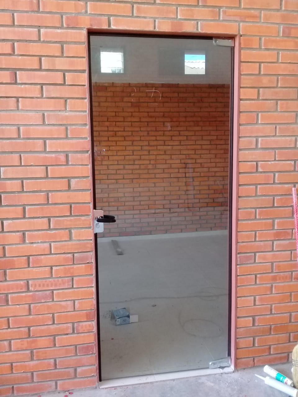 Puerta de vidrio templado con herrajes a la vista en vano de pared de ladrillo · MÁS VIDRIOS