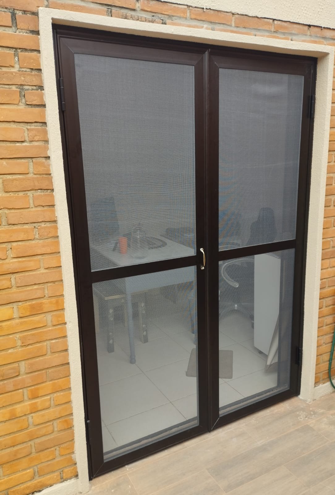 Puerta doble de aluminio con mosquitero instalada en muro de ladrillo visto · MÁS VIDRIOS