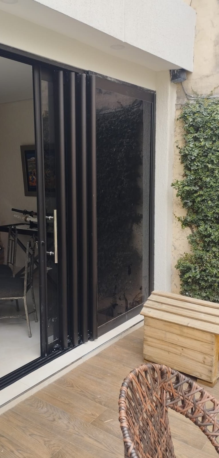 Puerta plegable de vidrio fumé con perfiles de aluminio oscuro en patio residencial · MÁS VIDRIOS