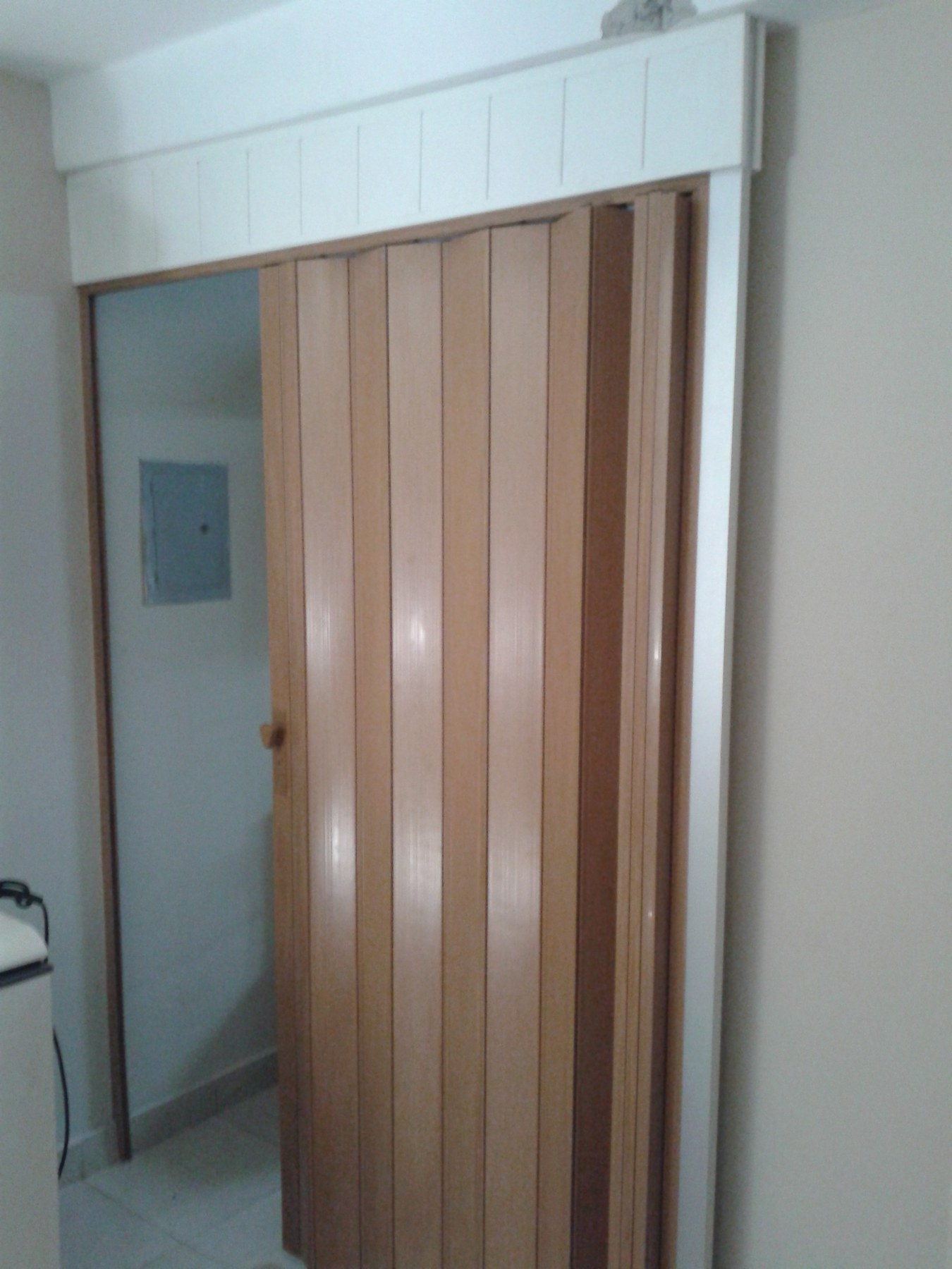 Puerta plegadiza de PVC en tono madera con marco y dintel blanco en un paso interior · MÁS VIDRIOS