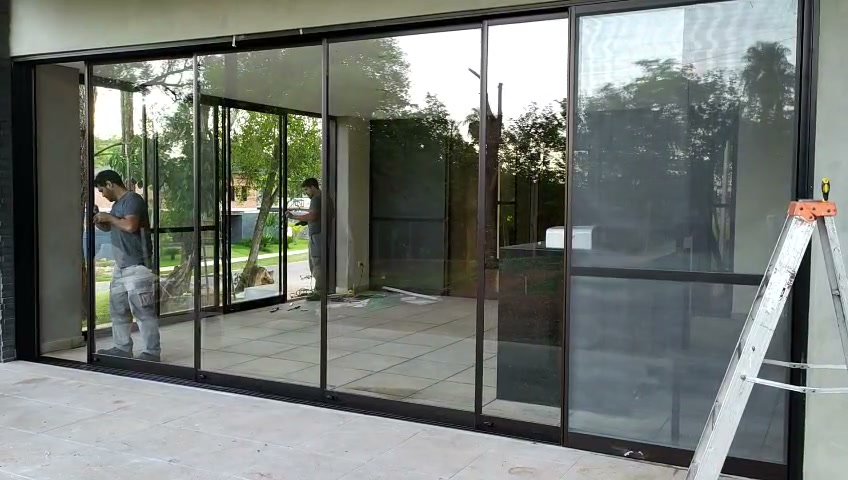 Frente corredizo de aluminio negro y vidrio cerrando la galería de una vivienda · MÁS VIDRIOS