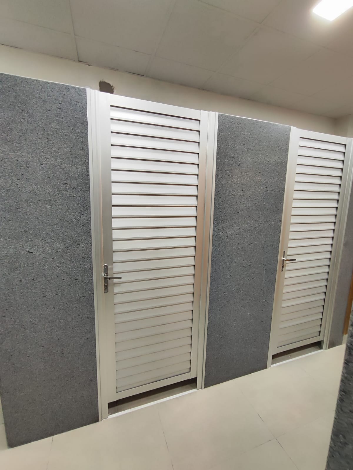 Puertas batientes de aluminio blanco con celosía completa entre paneles de granito · MÁS VIDRIOS