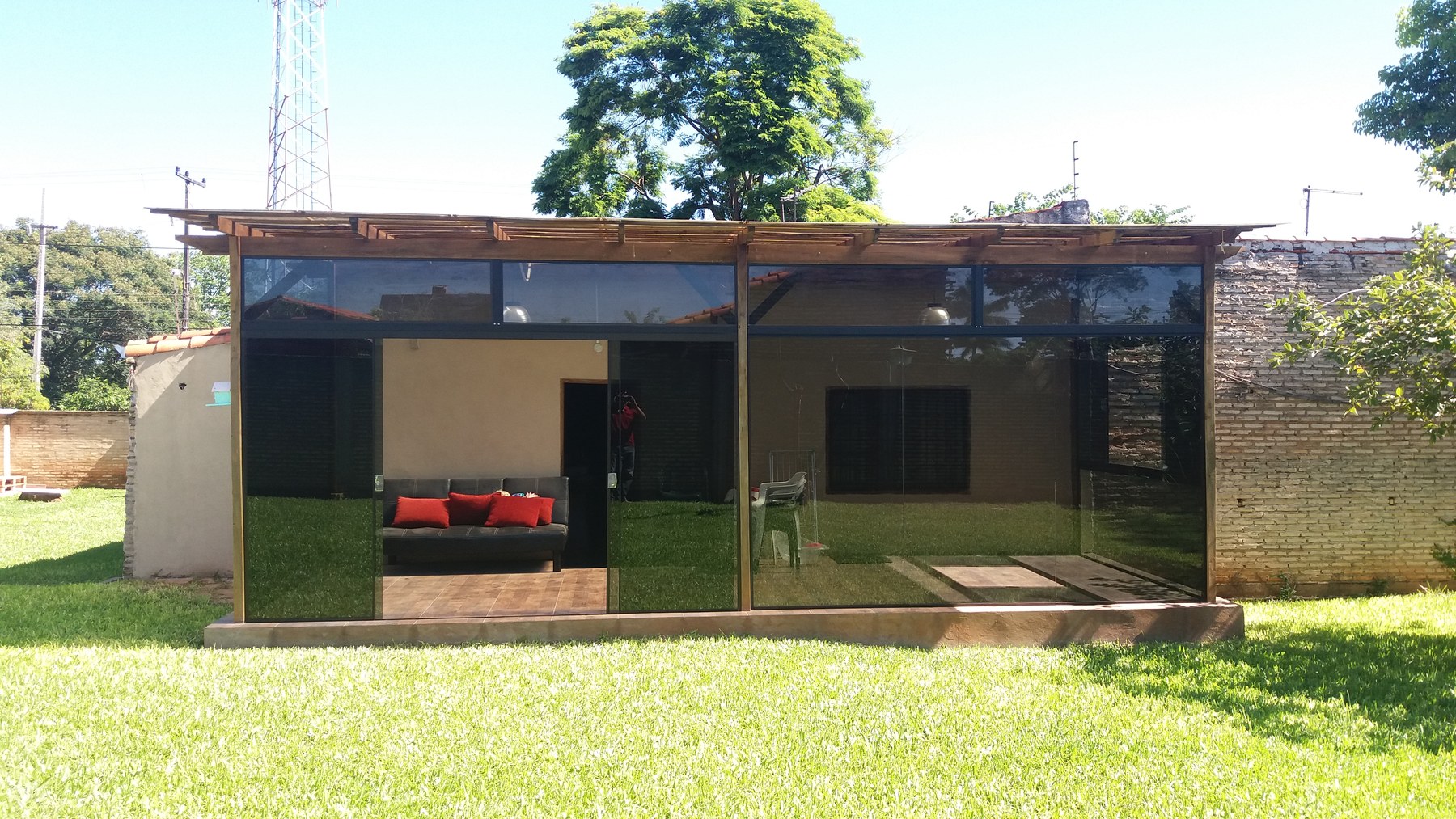 Quincho cerrado con paños de vidrio bajo techo de madera, visto desde el jardín · MÁS VIDRIOS