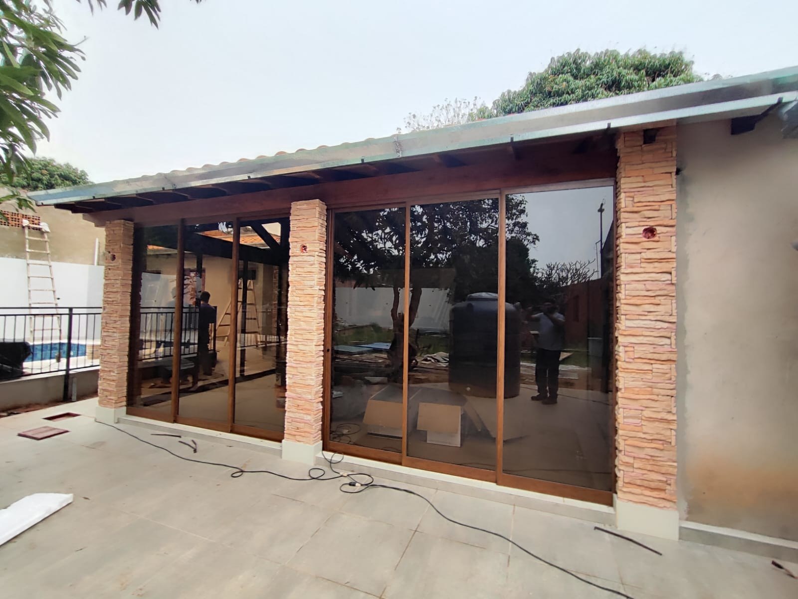 Galería cerrada con paños corredizos de aluminio símil madera y columnas de piedra · MÁS VIDRIOS