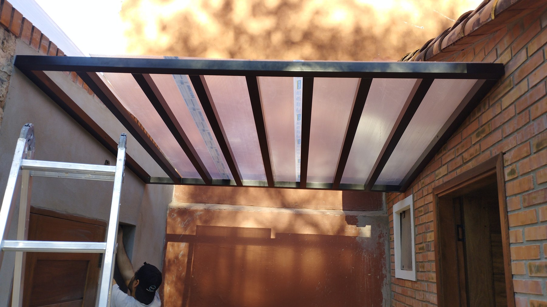 Techo de policarbonato con estructura metálica sobre el acceso de una casa · MÁS VIDRIOS