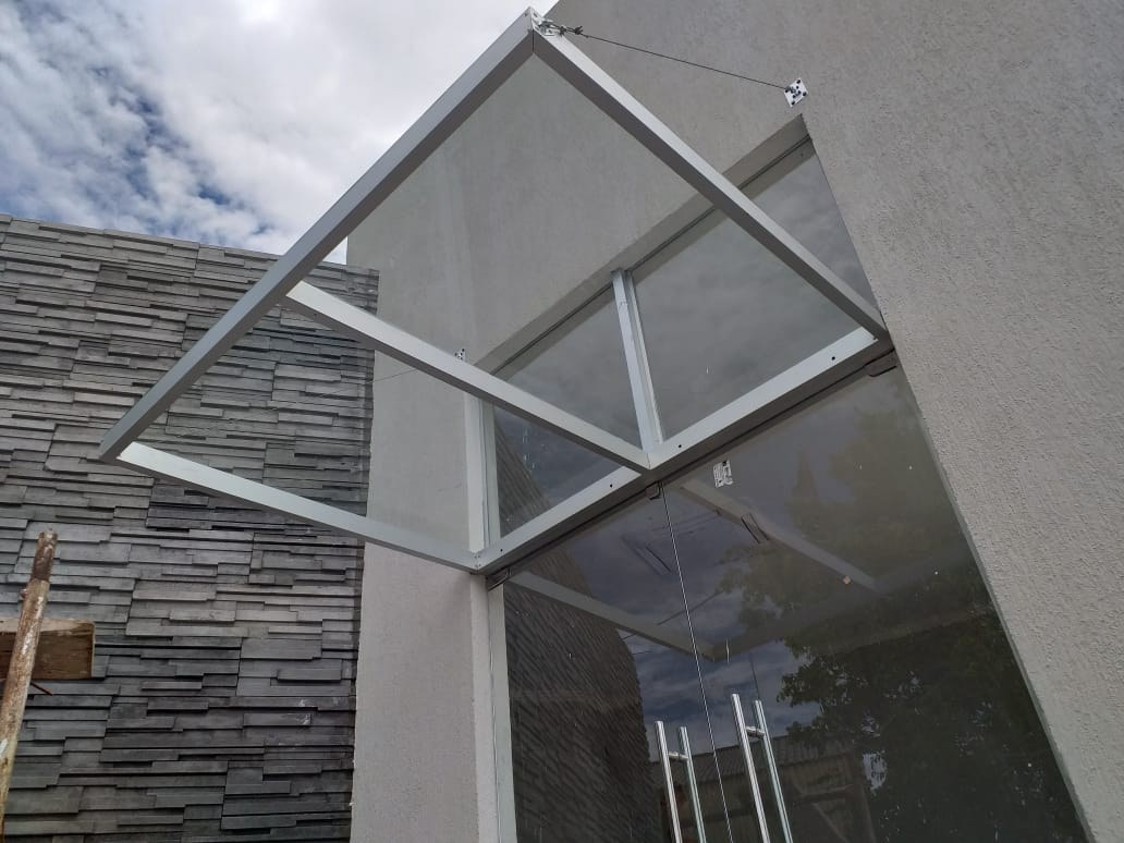 Techo de vidrio con estructura blanca sobre el acceso vidriado de una fachada de piedra · MÁS VIDRIOS