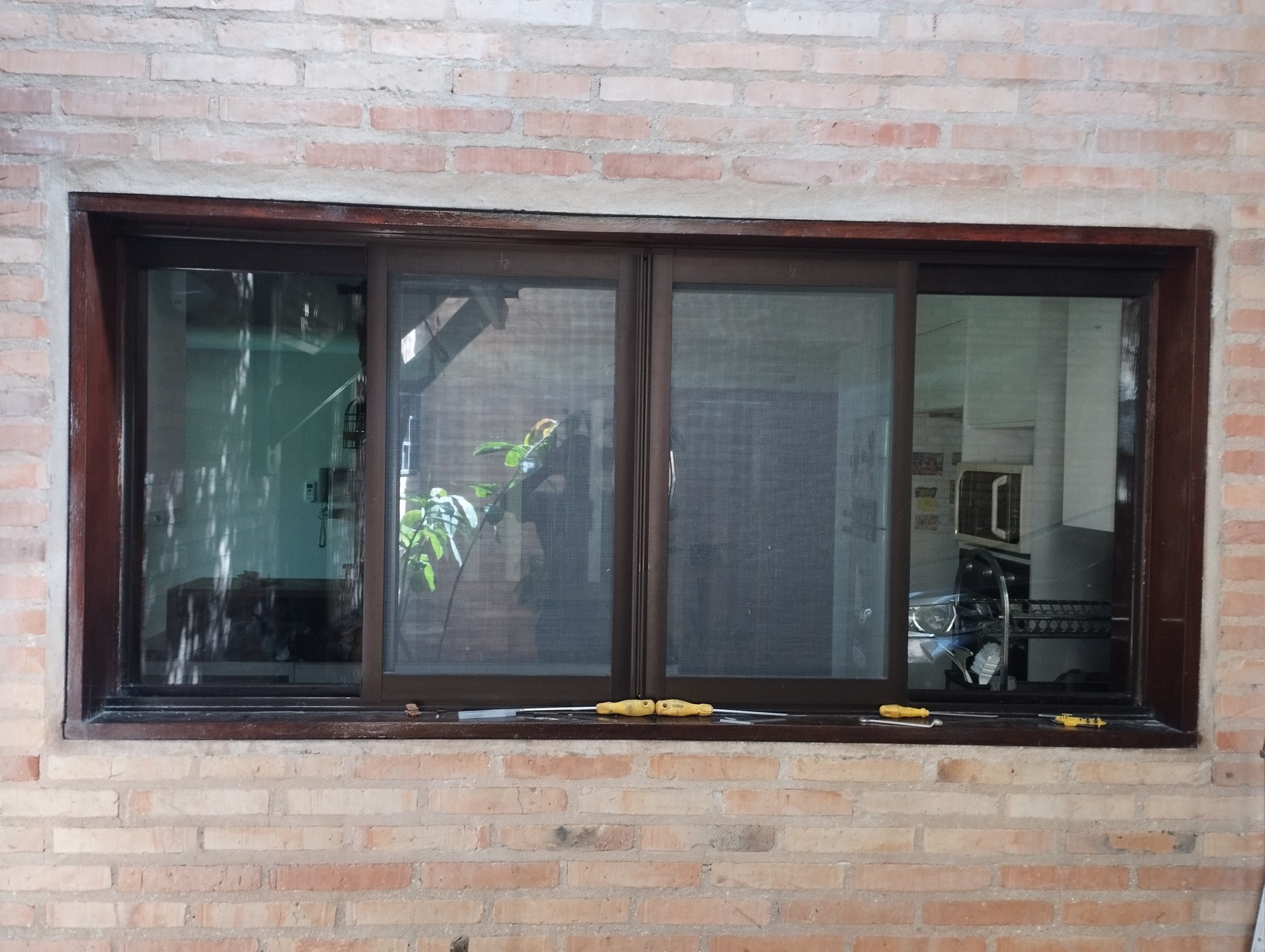 Ventana corrediza de aluminio marrón oscuro con mosquitero corredizo en pared de ladrillo visto · MÁS VIDRIOS