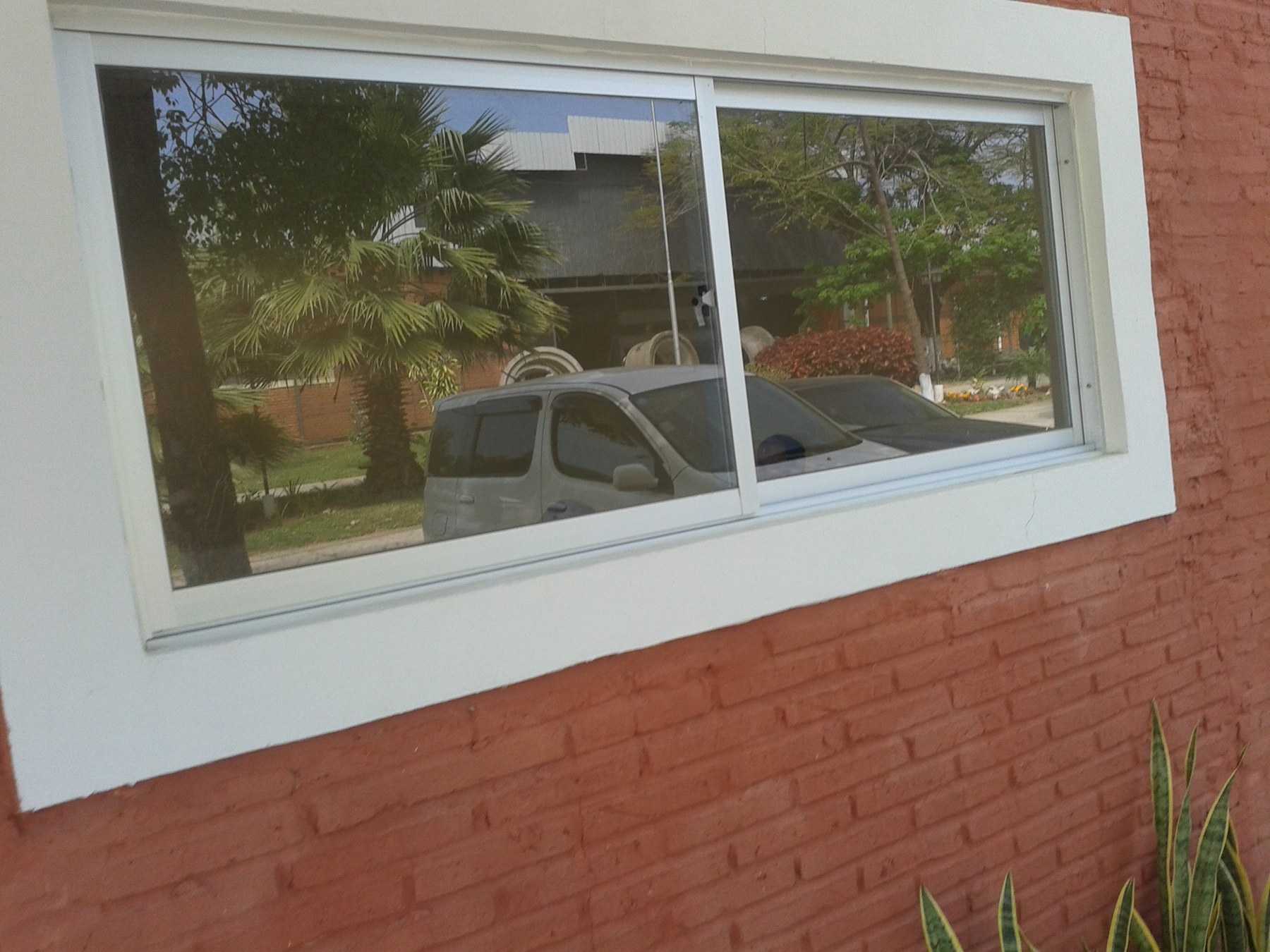 Ventana corrediza de aluminio blanco alargada sobre pared de ladrillo rojo · MÁS VIDRIOS