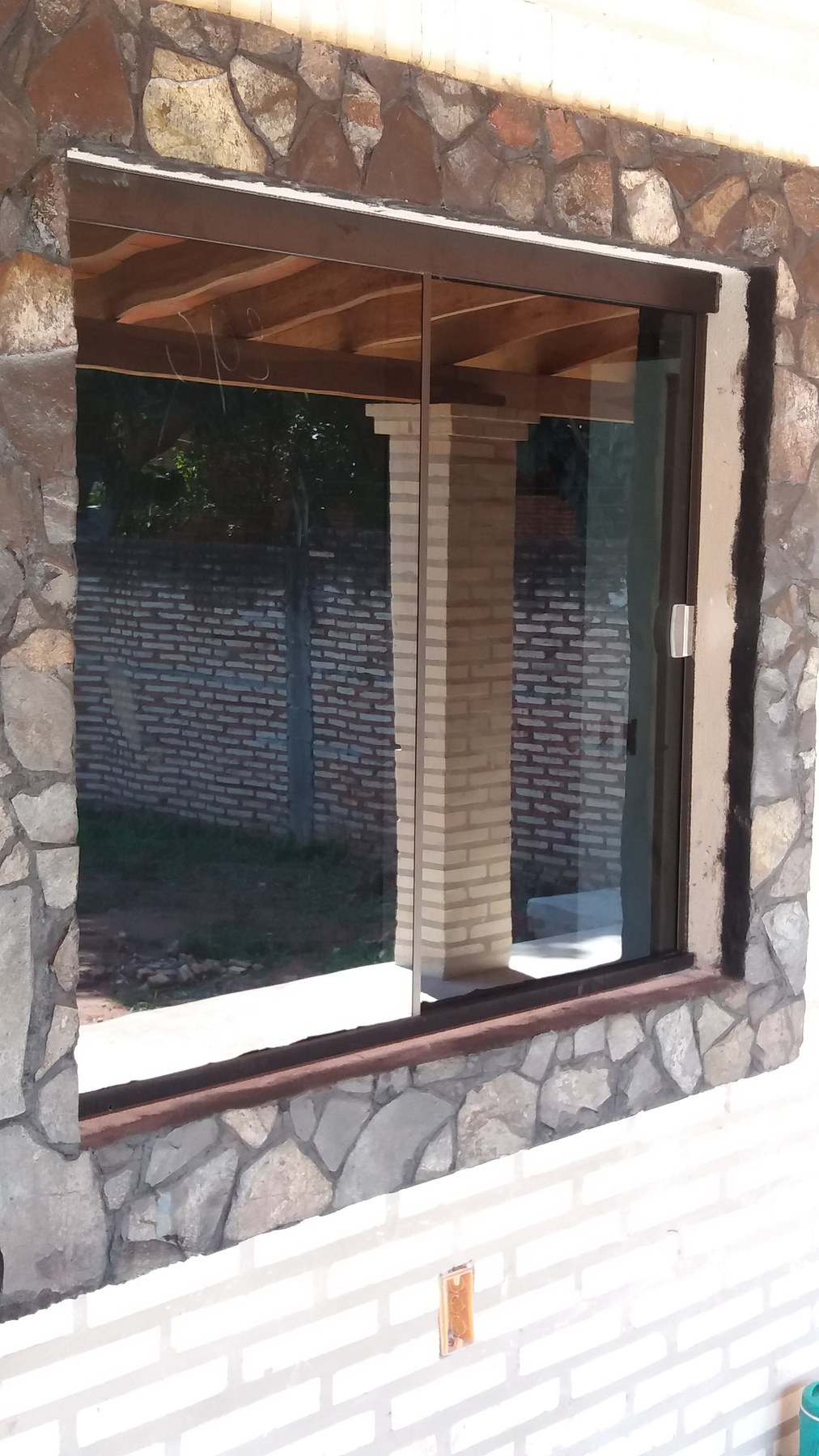 Ventana corrediza de aluminio color marrón en pared revestida en piedra · MÁS VIDRIOS