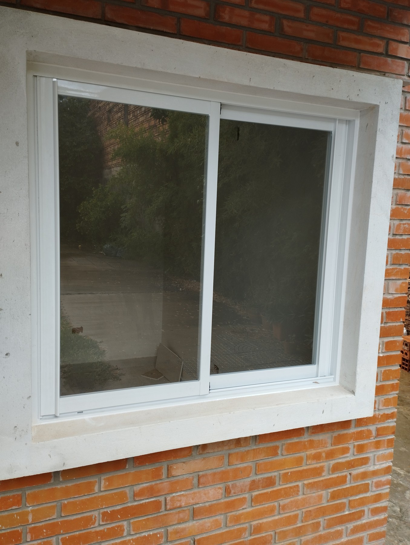 Ventana corrediza de aluminio blanco sobre pared de ladrillo visto · MÁS VIDRIOS