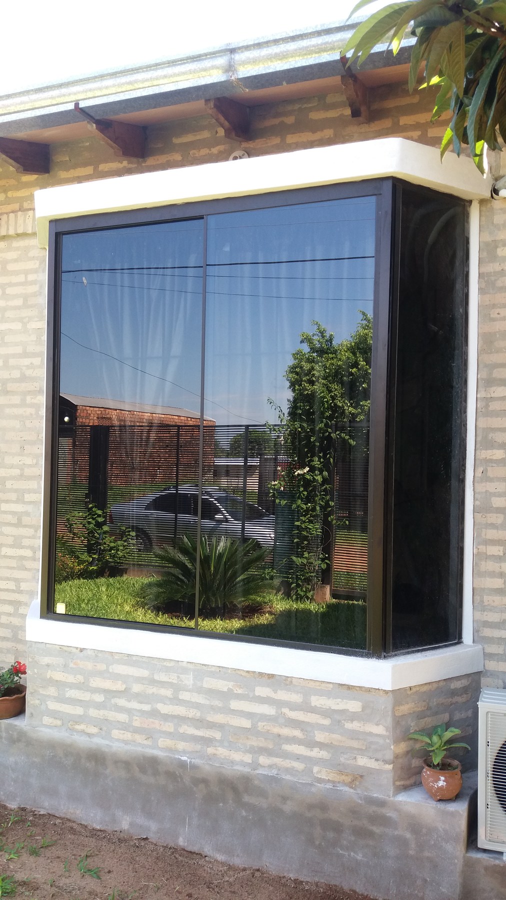 Ventana esquinera con vidrio tonalizado y perfilería de aluminio en fachada de ladrillo · MÁS VIDRIOS
