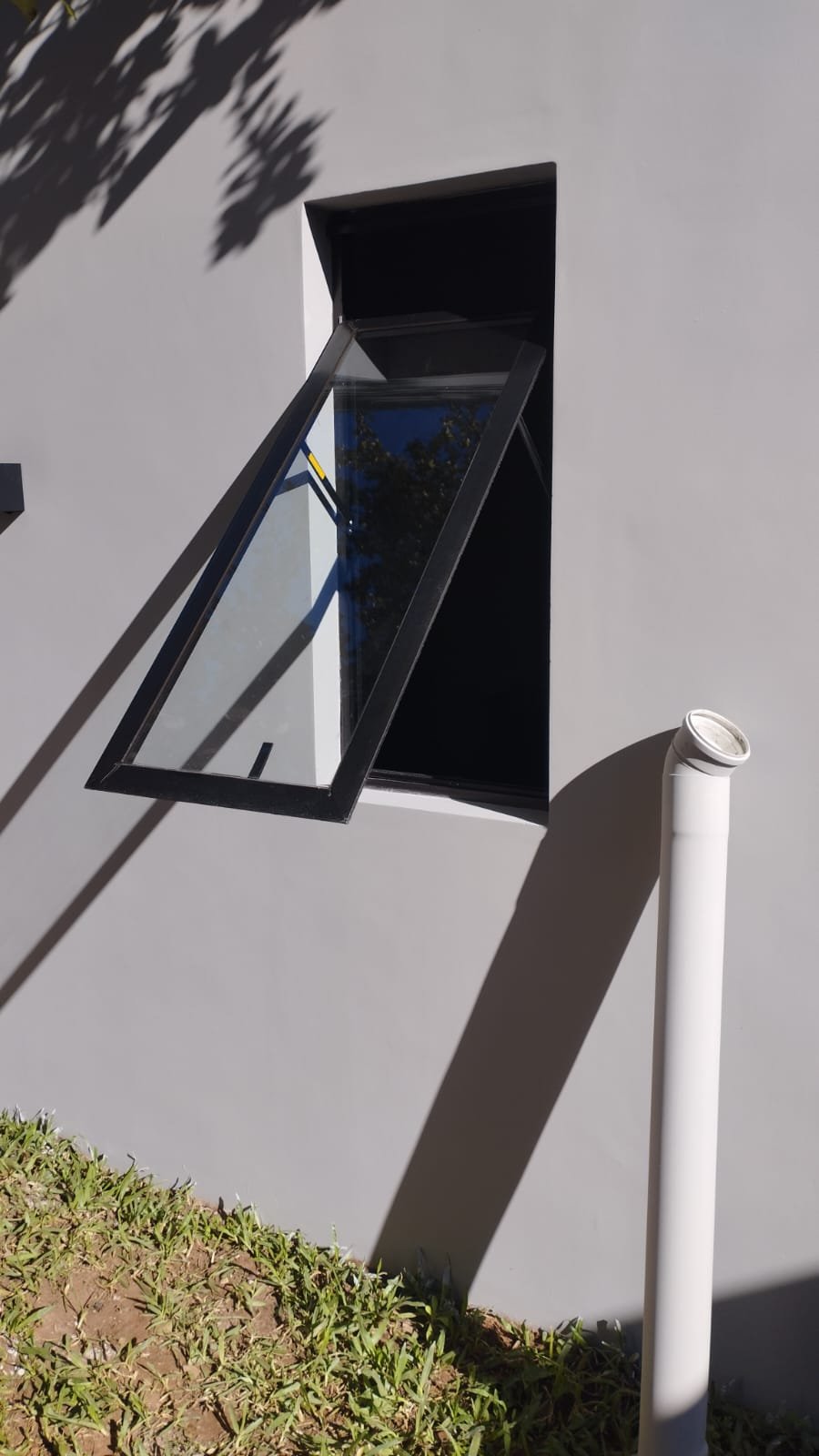 Ventana proyectante de aluminio negro instalada en fachada residencial · MÁS VIDRIOS