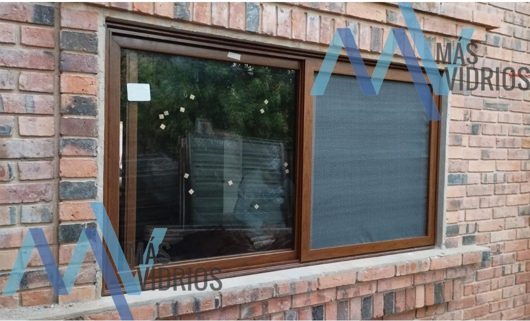 Ventana corrediza de aluminio símil madera con mosquitero sobre pared de ladrillo visto · MÁS VIDRIOS