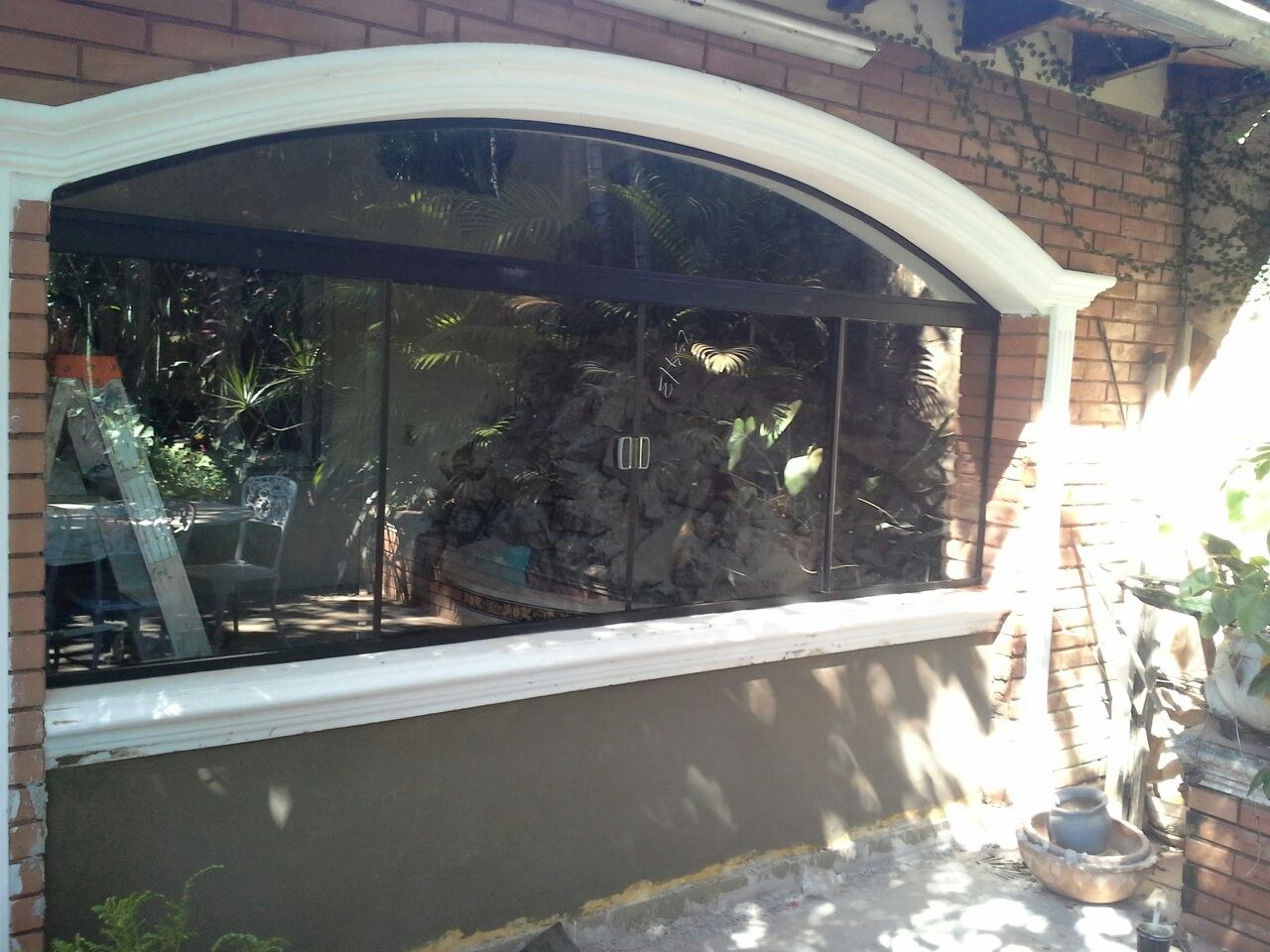 Ventanal arqueado con perfilería de aluminio oscuro en la galería de una vivienda · MÁS VIDRIOS