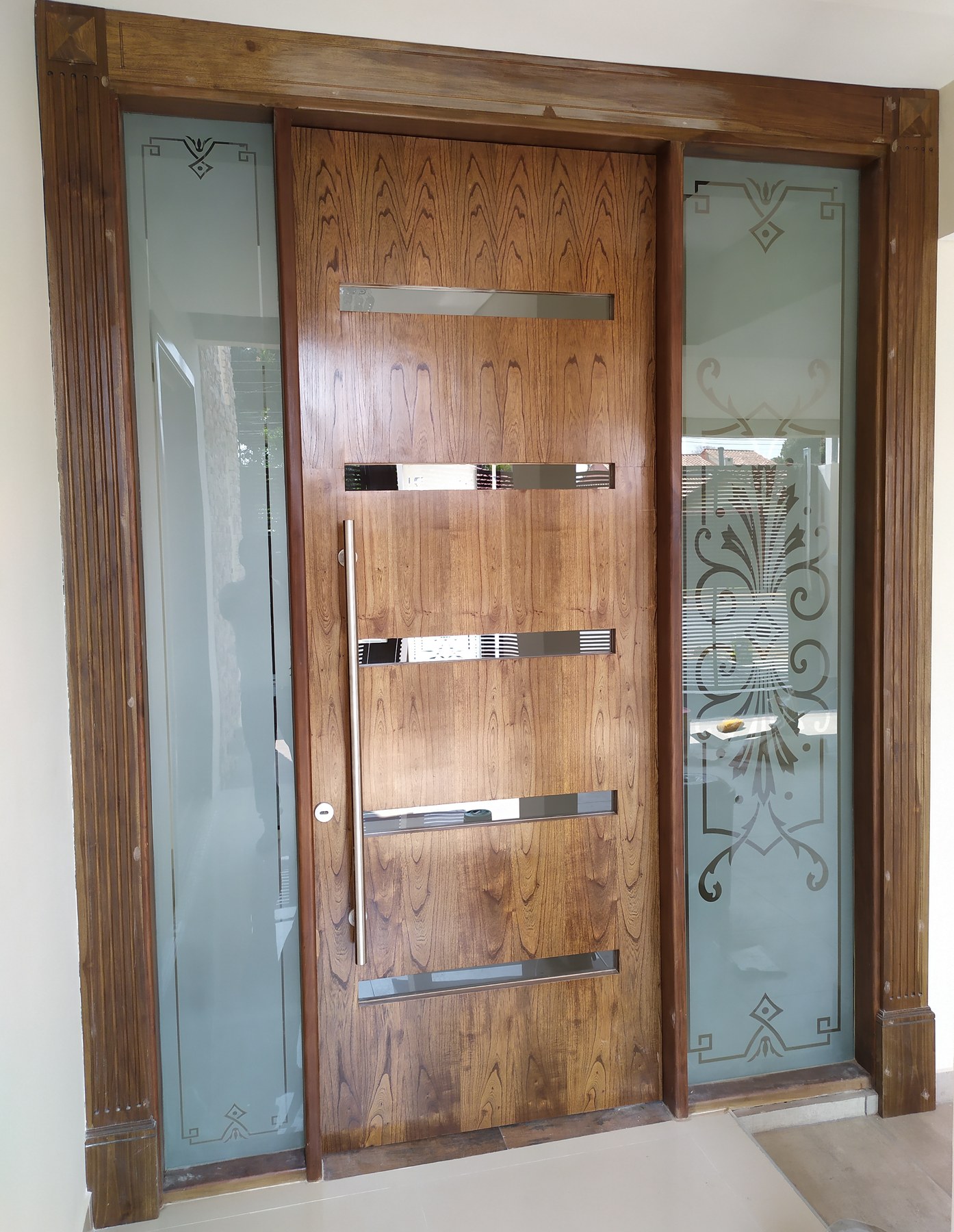 Paños de vidrio ploteado con diseño de guardas a los lados de una puerta de madera · MÁS VIDRIOS