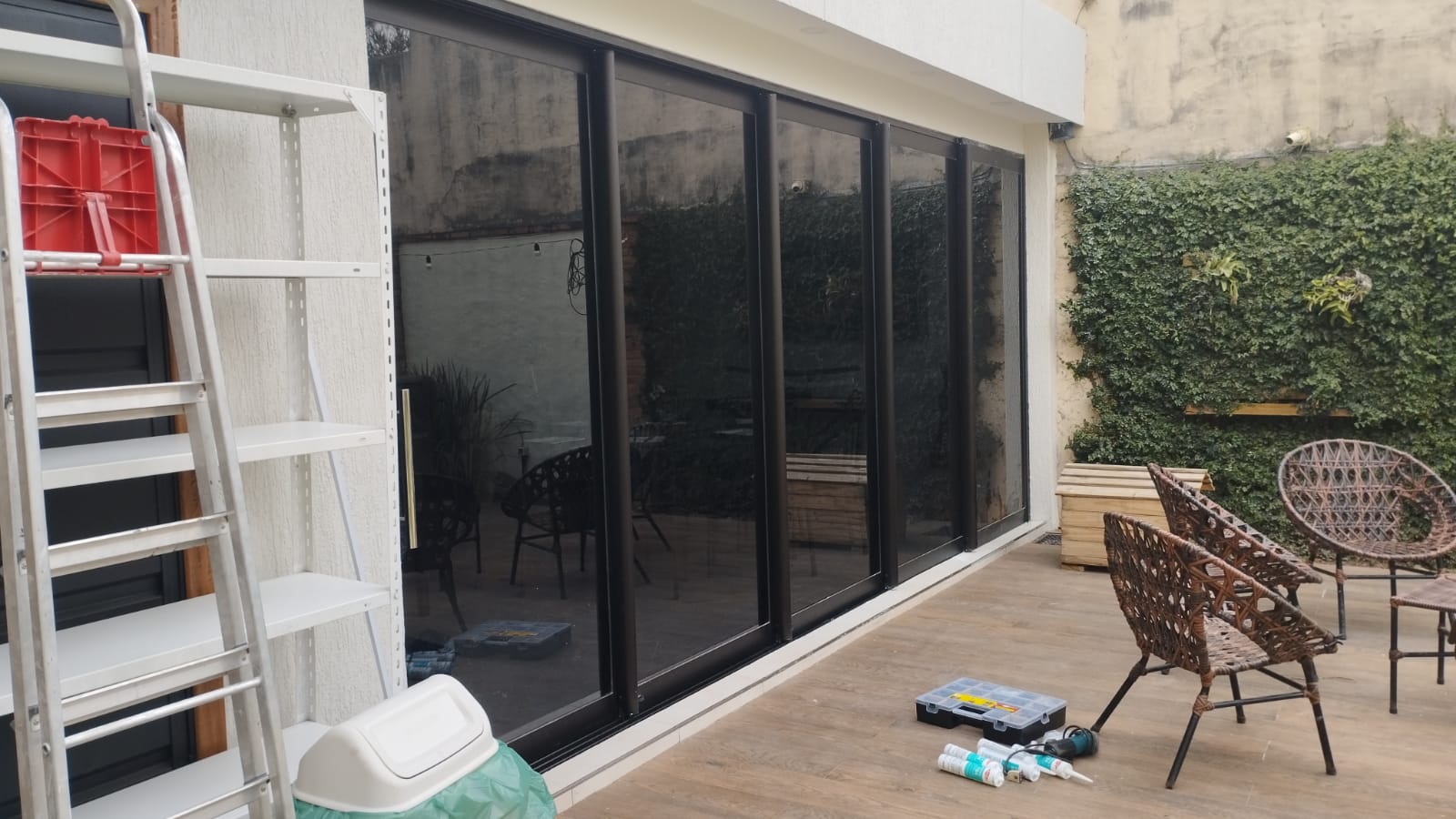 Puerta corrediza de vidrio con aluminio negro hacia patio con jardín vertical · MÁS VIDRIOS