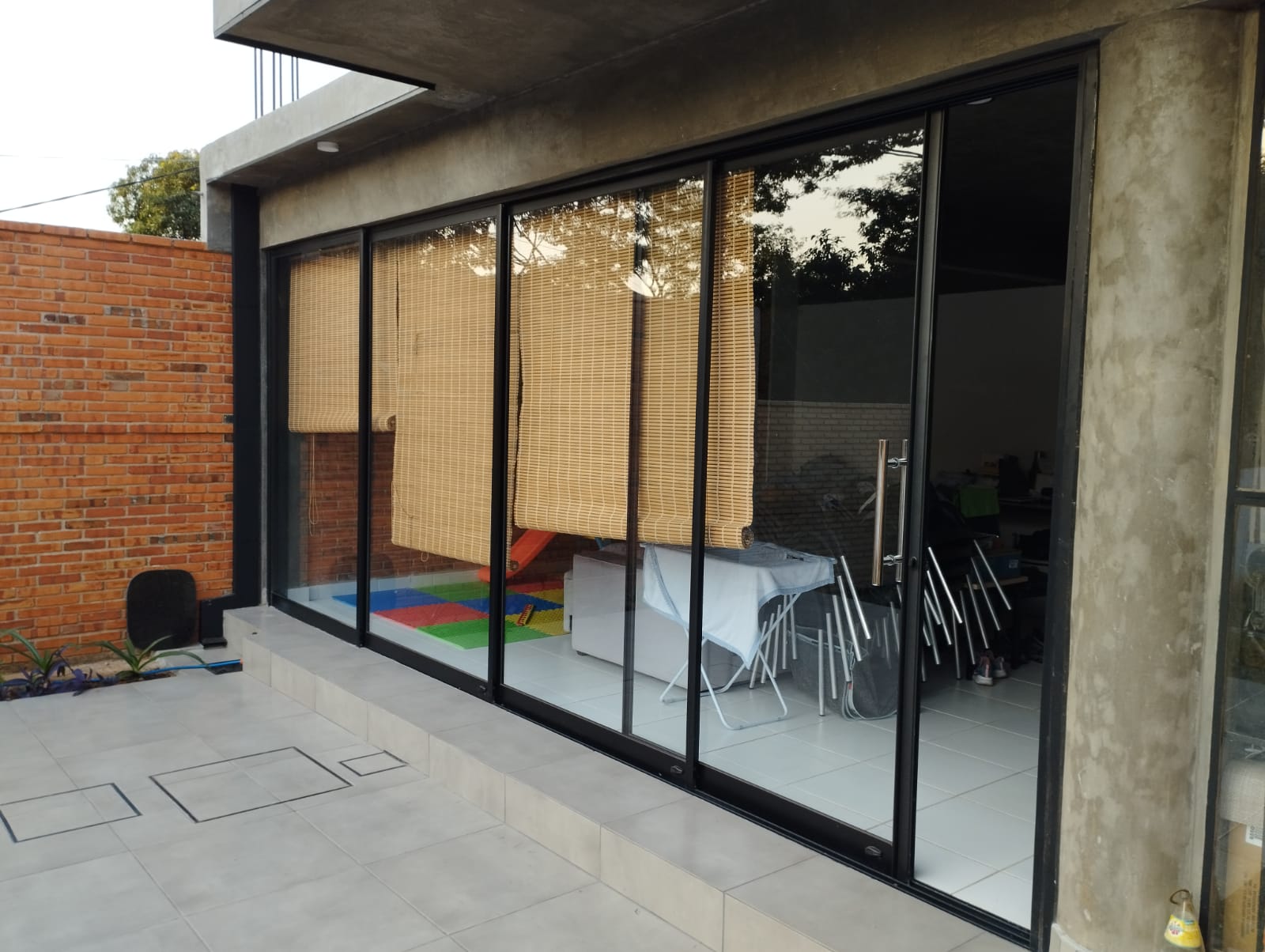 Cerramiento de vidrio corredizo con aluminio negro en patio con muro de ladrillo · MÁS VIDRIOS